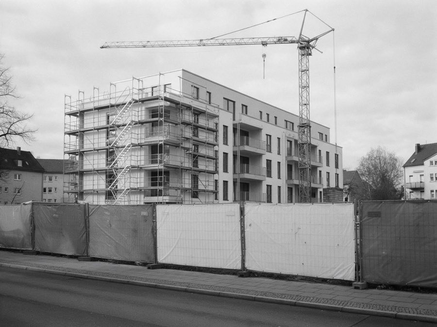 Bauzaun mit weißen Planen vor einem Neubau, schwarzweiß